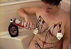 Busty brunette bathes with chocolate sauce and whipped cream on her tits