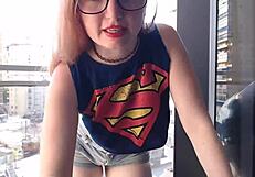 A hot gamer girl in clothes flashes her big tits on the balcony outdoors